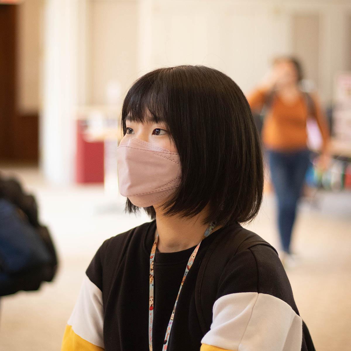 图为一名戴着口罩参加国际活动的学生