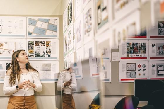 图为波胆网站的一名女学生抬头看着挂在墙上的打印出来的设计项目. 
