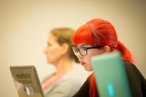 Photo of a female Chatham University student writing on her laptop during a lecture.