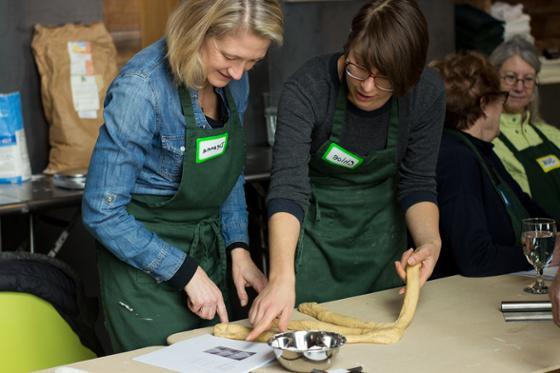 图为一名妇女在伊甸堂校园帮助另一名妇女制作查拉面包
