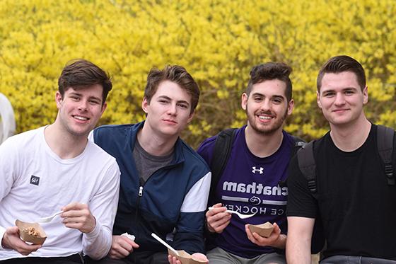 Photo of four male Chatham University students posing together outside smiling and eating ice cream