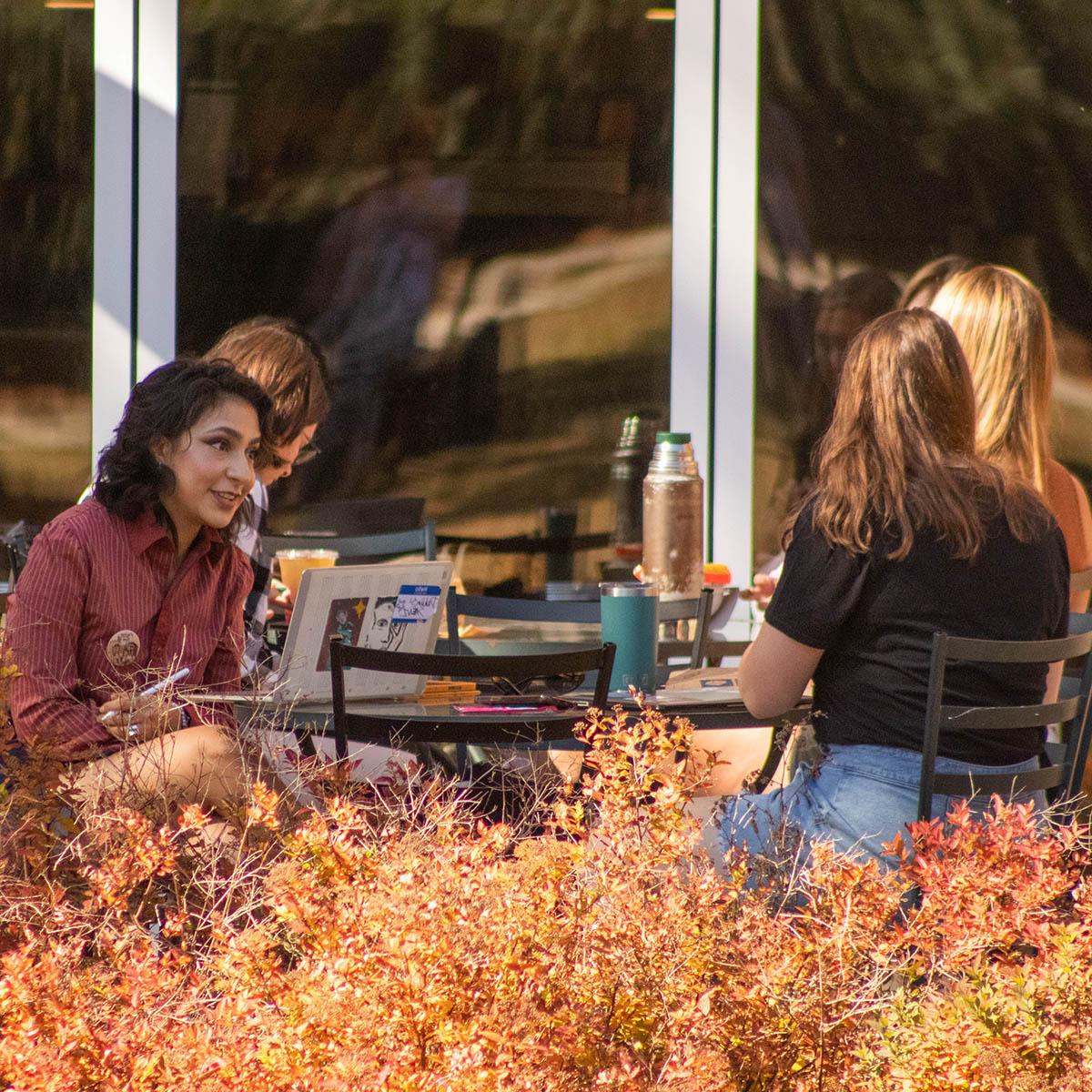 学生们坐在户外瑞秋咖啡馆的桌旁，前景是秋天的树叶