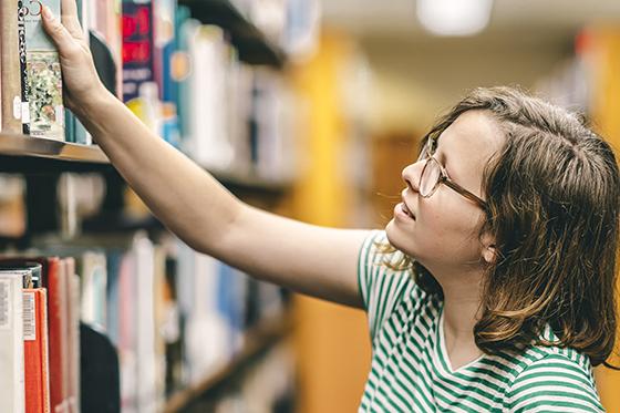 图为波胆网站的一名女学生从图书馆书架上取下一本书